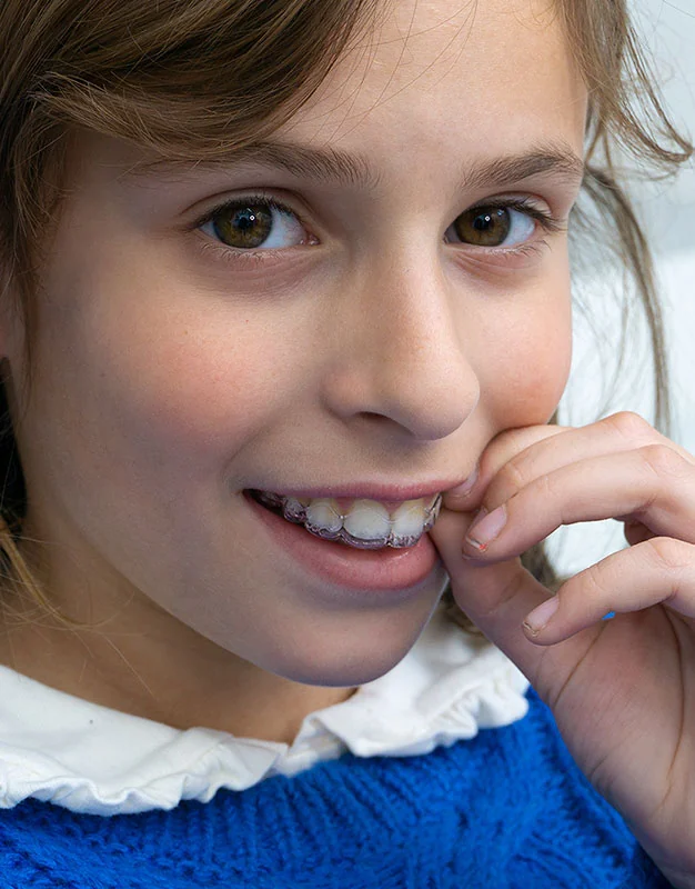 Ragazza che sorride mentre tiene un allineatore trasparente davanti ai denti.