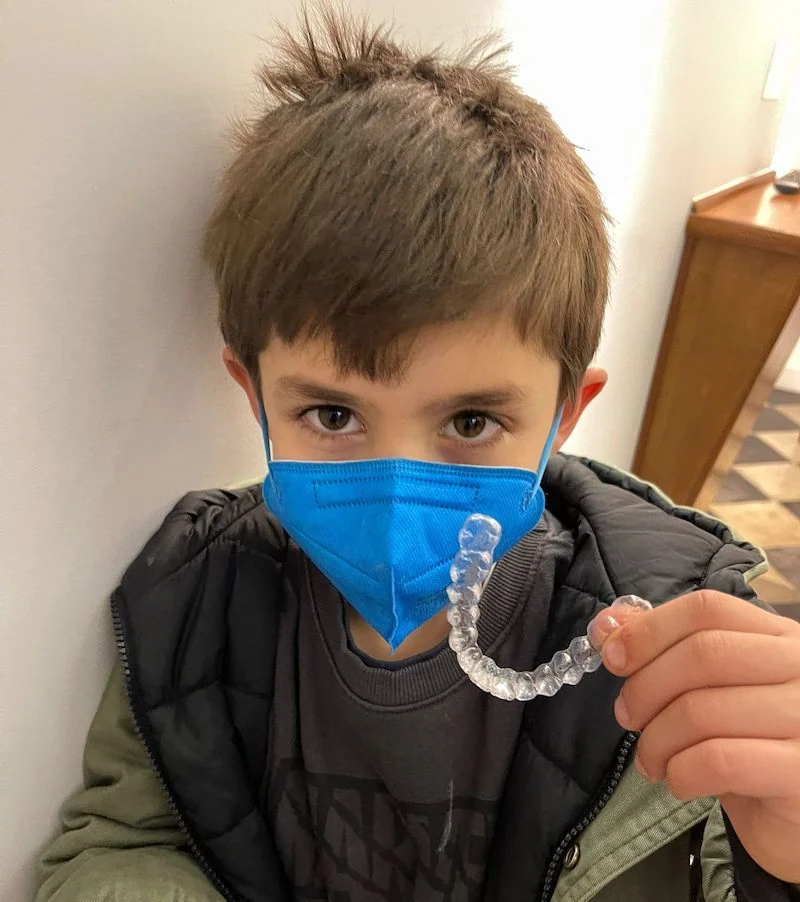 Bambino con mascherina sanitaria che mostra un allineatore trasparente.