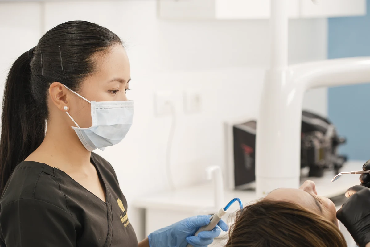 Professionista con mascherina e guanti accanto alla paziente durante una seduta odontoiatrica.